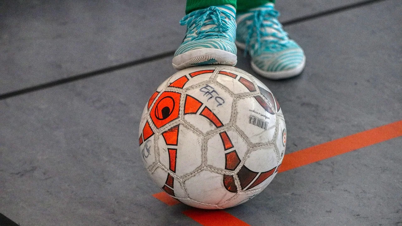Jogadores disputam a bola em uma quadra de futsal.