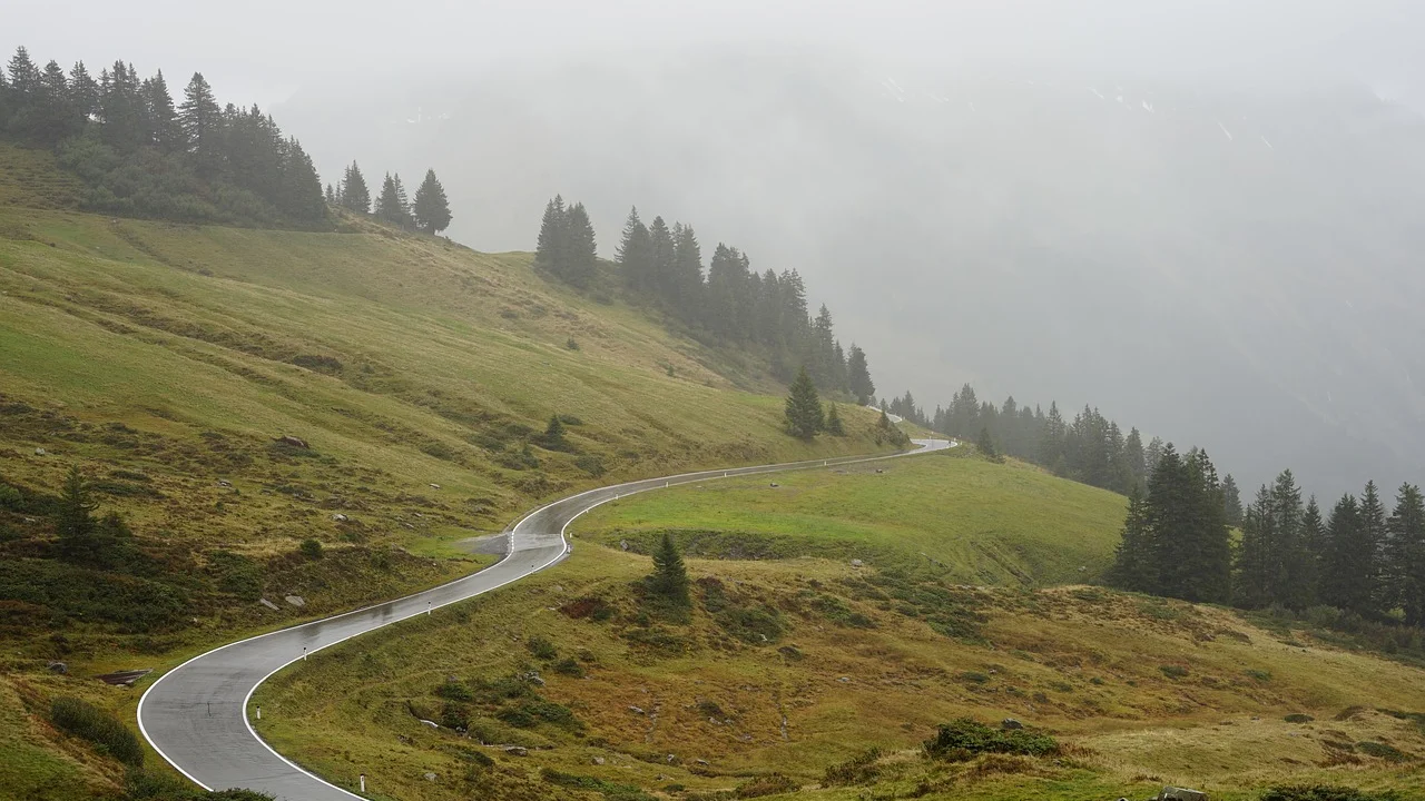 Carro percorre uma rodovia sinuosa em região montanhosa.