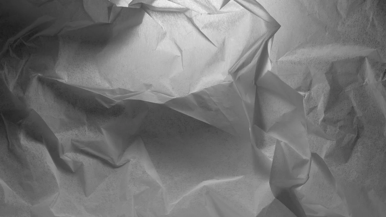 Mãos alinhando as pontas de um papel quadrado.