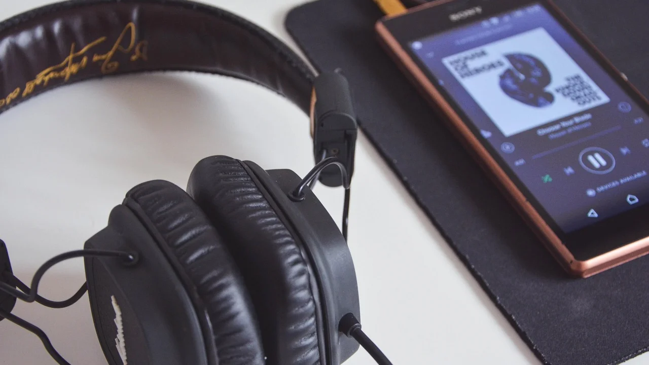 Fones de ouvido ao lado de um celular com playlist aberta