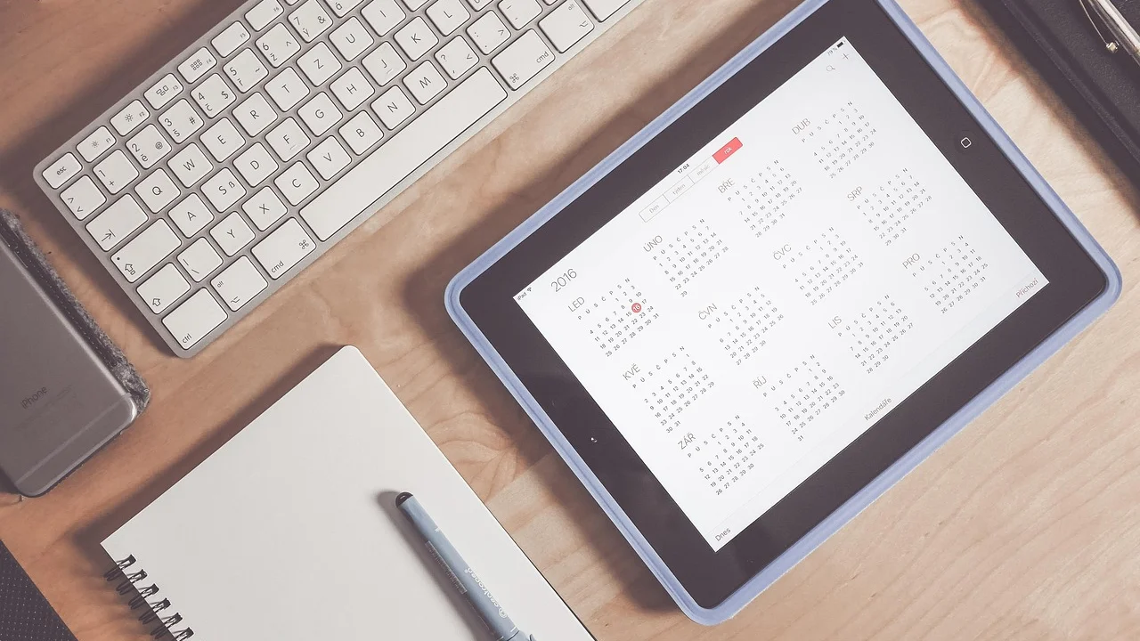 Mesa de trabalho com caderno, celular e calendário aberto.